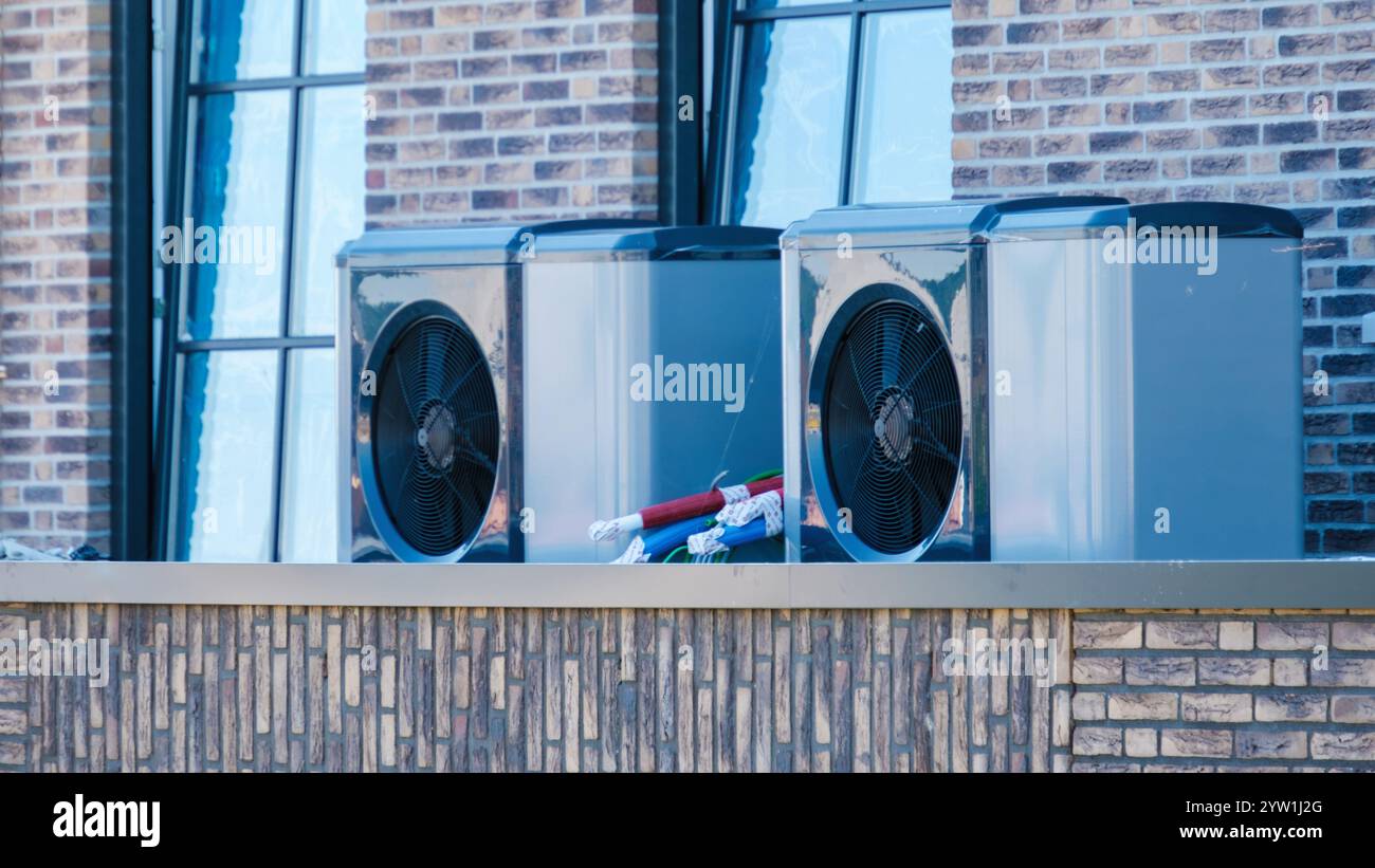 Trois pompes à chaleur à air épurées sont installées sur un toit aux pays-Bas, reflétant la lumière du soleil matinal dans un cadre résidentiel contemporain. Banque D'Images