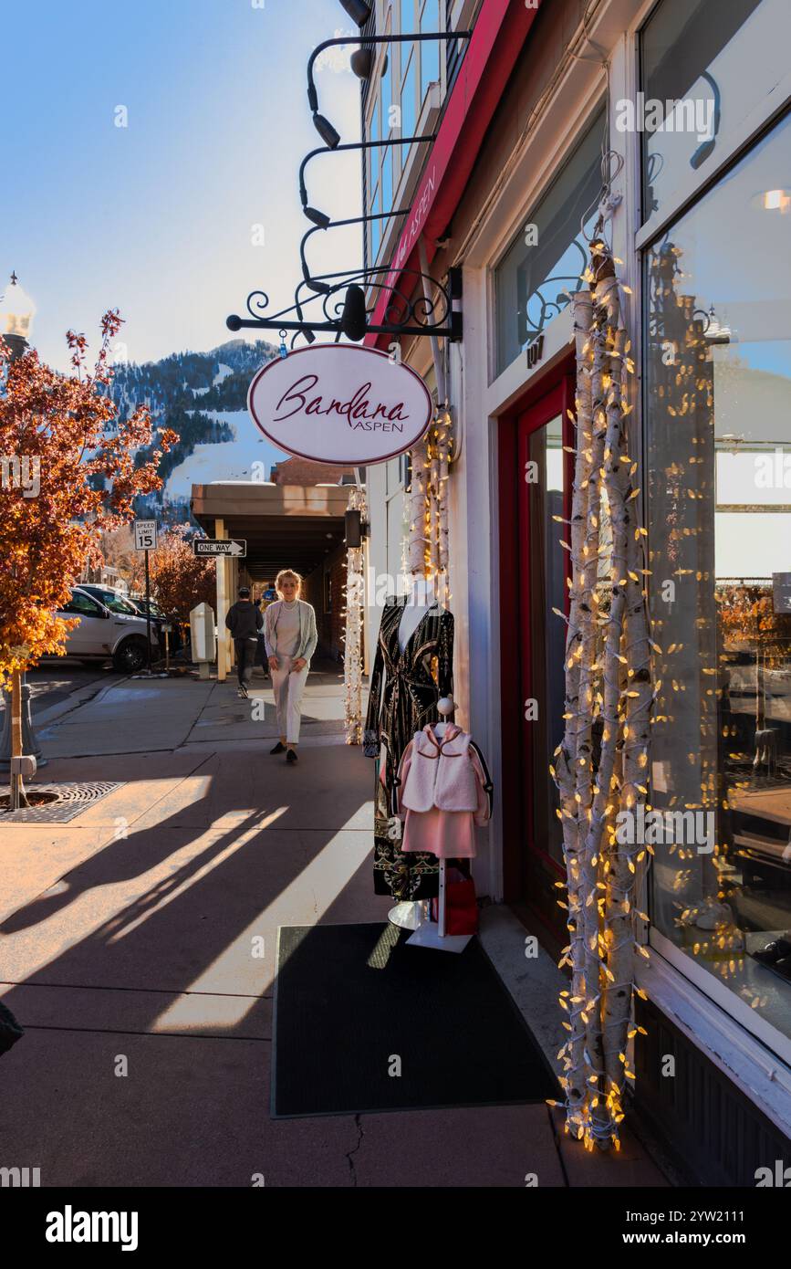Scène de trottoir avec vitrine et enseigne suspendue pour Bandana Aspen, femme bien habillée sur le trottoir, début de l'hiver, centre-ville d'Aspen, Colorado, USA. Banque D'Images