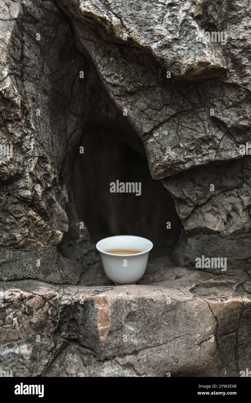 Une scène sereine et apaisante avec une tasse de thé délicate reposant doucement sur une surface rocheuse, symbolisant la vraie tranquillité Banque D'Images