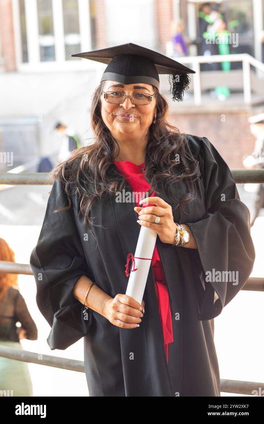 Femme souriante en robe de graduation et casquette détenant un diplôme avec un ruban rouge, Bournemouth, Dorset UK Banque D'Images