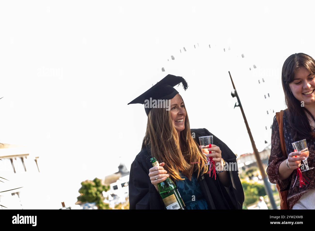 Célébration de la remise des diplômes avec une femme souriante en casquette, tenant une bouteille de champagne, accompagnée d'une autre femme tenant un verre, Bournemouth, Dorset UK Banque D'Images