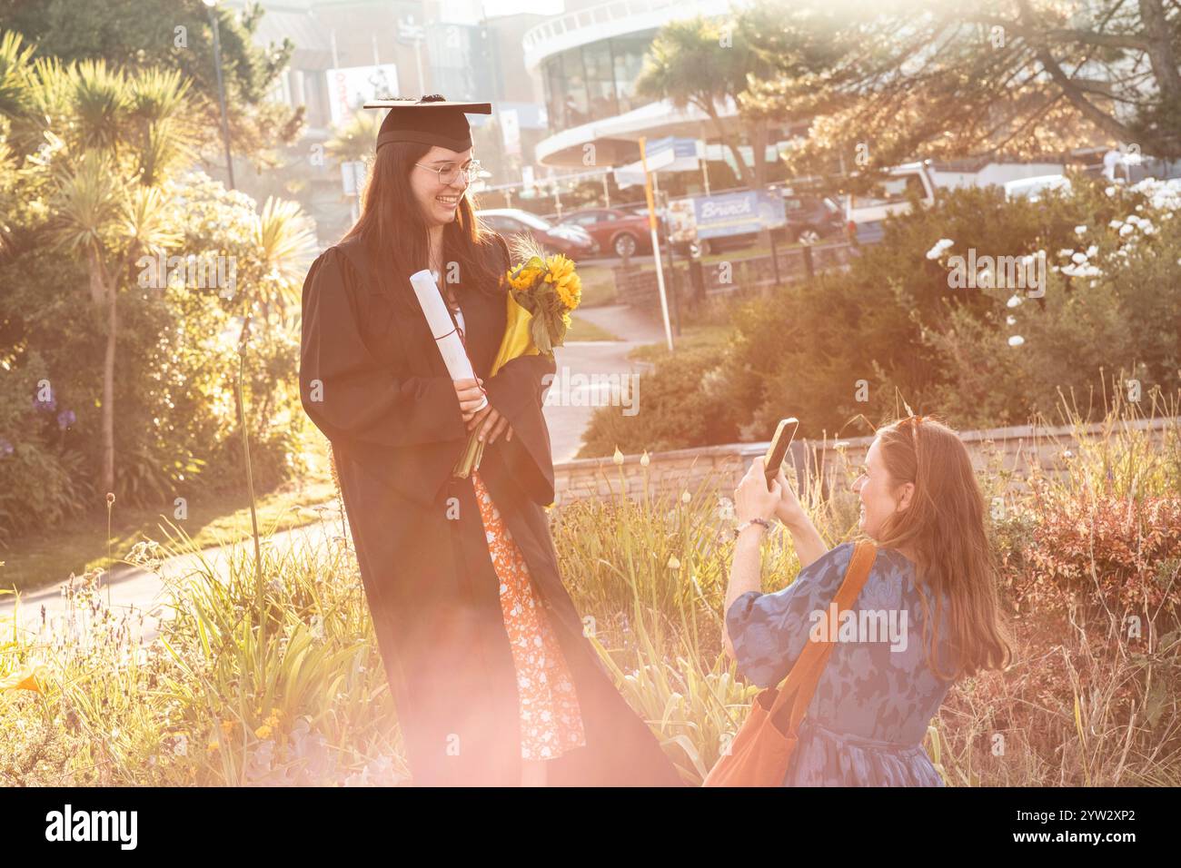 Diplômée titulaire d'un diplôme et des fleurs sourient tandis qu'une autre personne prend sa photo dans un jardin ensoleillé, Bournemouth, Dorset UK Banque D'Images