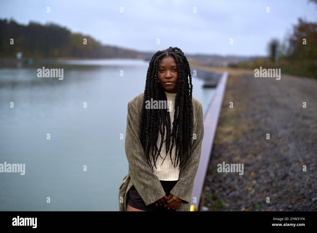 Une jeune femme réfléchie avec de longs cheveux tressés debout près d'un lac pendant le crépuscule, Brandebourg, Allemagne Banque D'Images