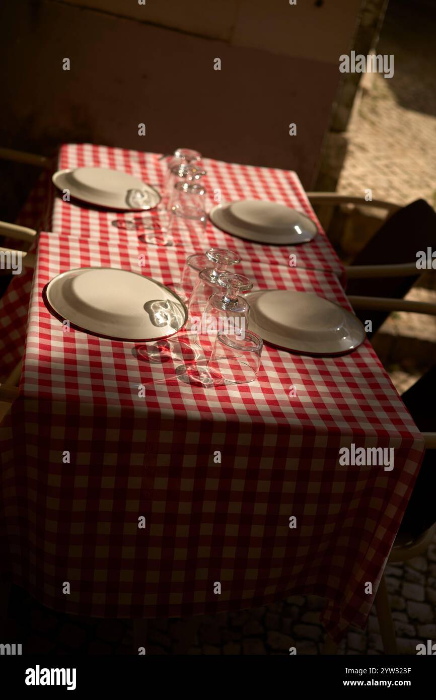 Une configuration de salle à manger en plein air confortable avec une nappe à carreaux rouge et blanc, des assiettes blanches vides et des verres transparents sous éclairage naturel, Portugal Banque D'Images