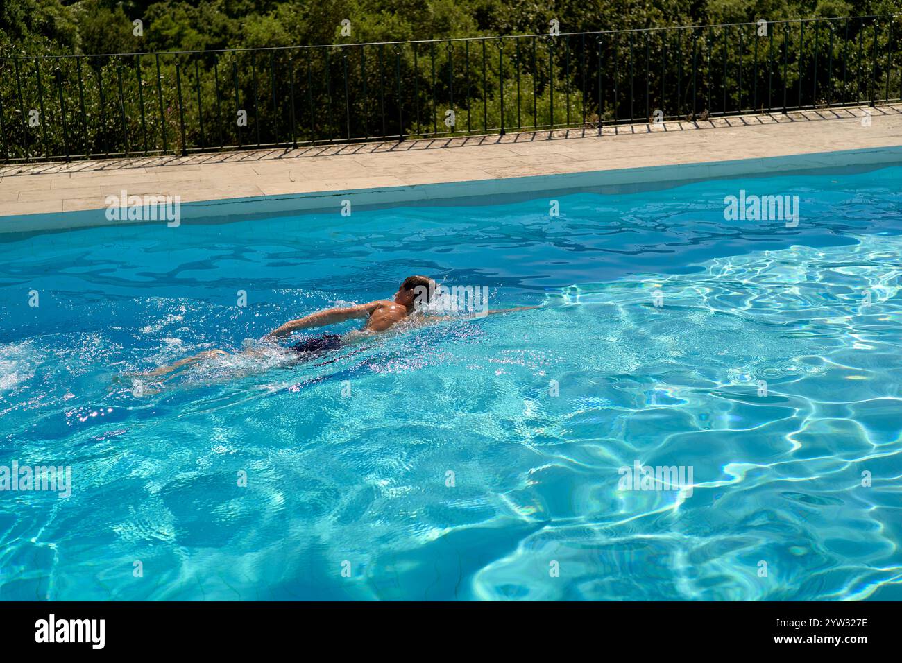 Adolescent nageant freestyle dans une piscine extérieure claire sur une journée ensoleillée avec des arbres en arrière-plan, Portugal Banque D'Images