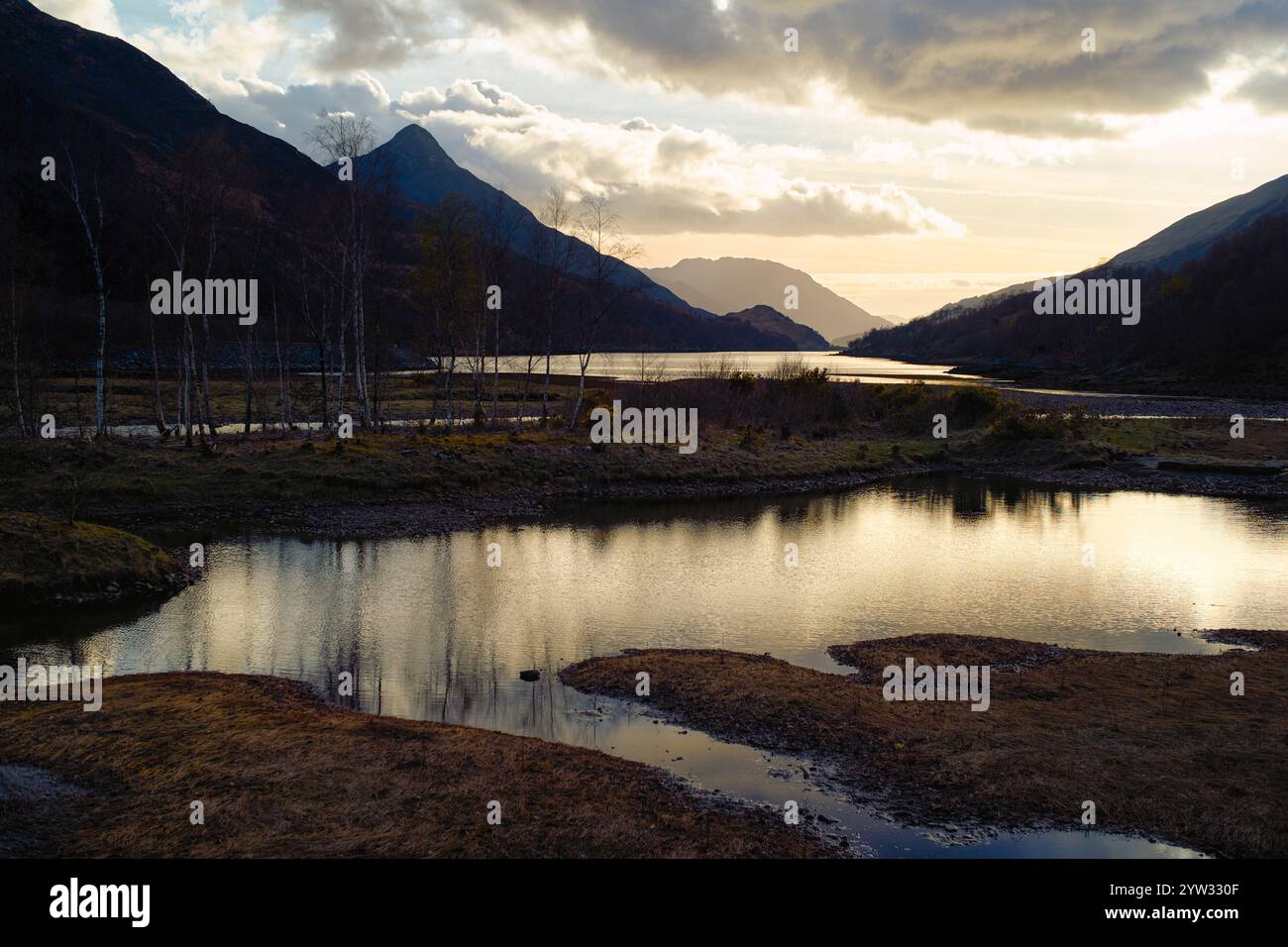 Coucher de soleil sur un paysage de montagne serein avec un plan d'eau réfléchissant et des nuages éparpillés, Highlands, Écosse Banque D'Images
