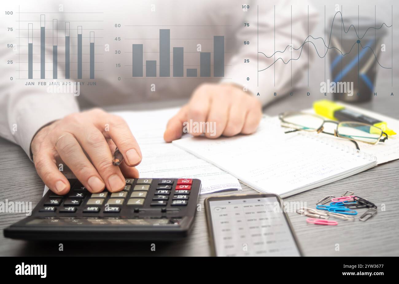Calculer les dépenses et analyser les données financières dans un espace de travail professionnel avec notes et papeterie à proximité pour référence. Banque D'Images