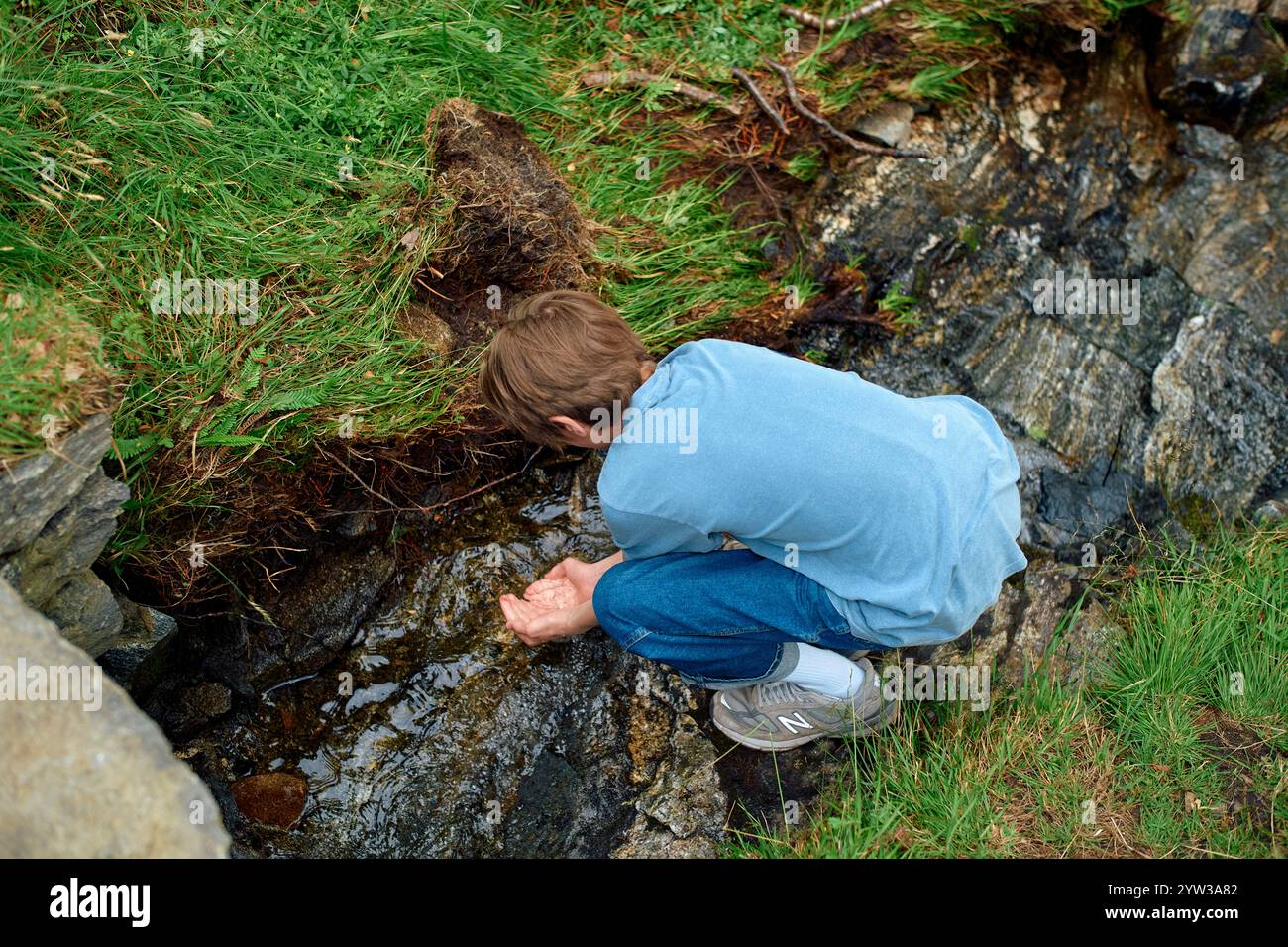 Adolescent dans une chemise bleue ramassant de l'eau d'un ruisseau de montagne clair, Romsdalfjorden, Norvège Banque D'Images