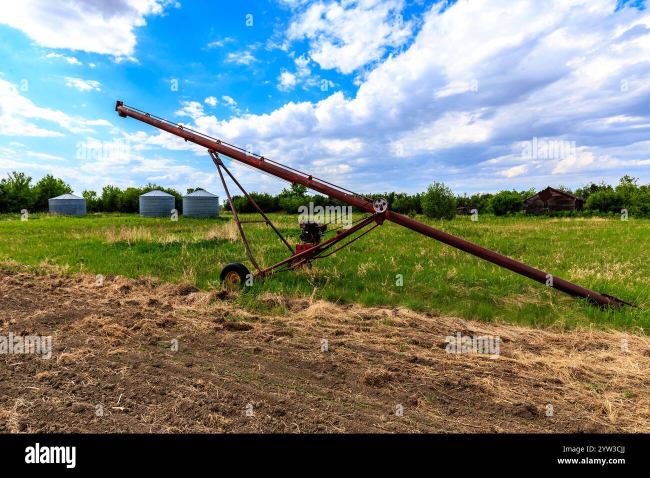 Un tracteur rouge et jaune est assis dans un champ. Le tracteur est vieux et rouillé. Le ciel est bleu et il y a quelques nuages Banque D'Images