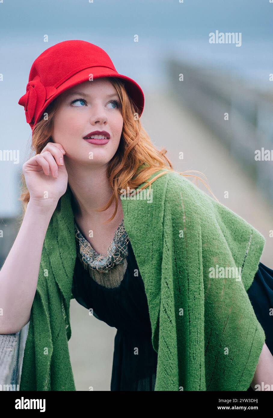 Femme élégante dans un chapeau rouge et châle vert regardant soigneusement au loin. Banque D'Images