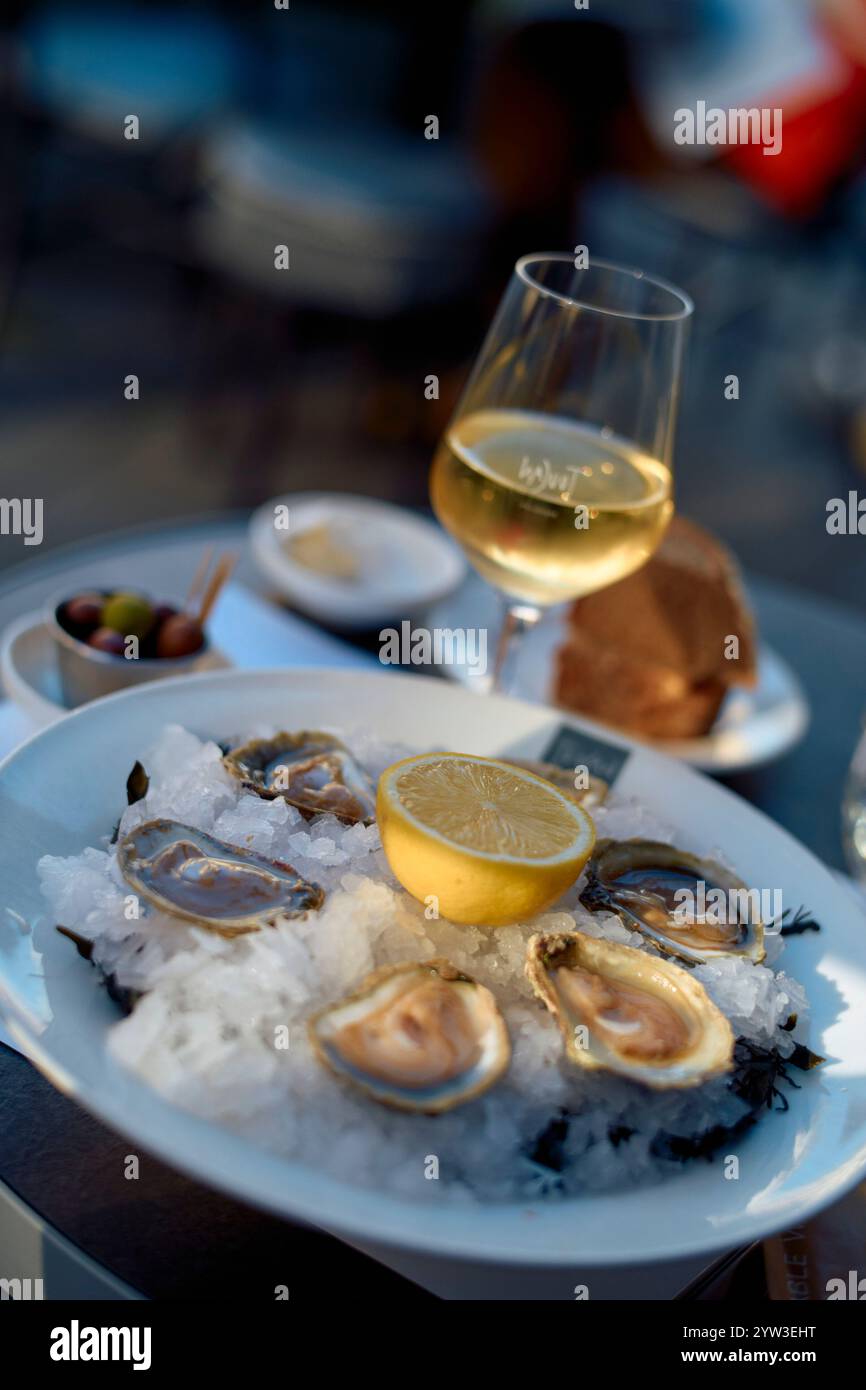Huîtres fraîches sur glace avec citron accompagnées d'un verre de vin blanc, de pain et d'olives sur une table en plein air, rivière Moselle, Allemagne Banque D'Images