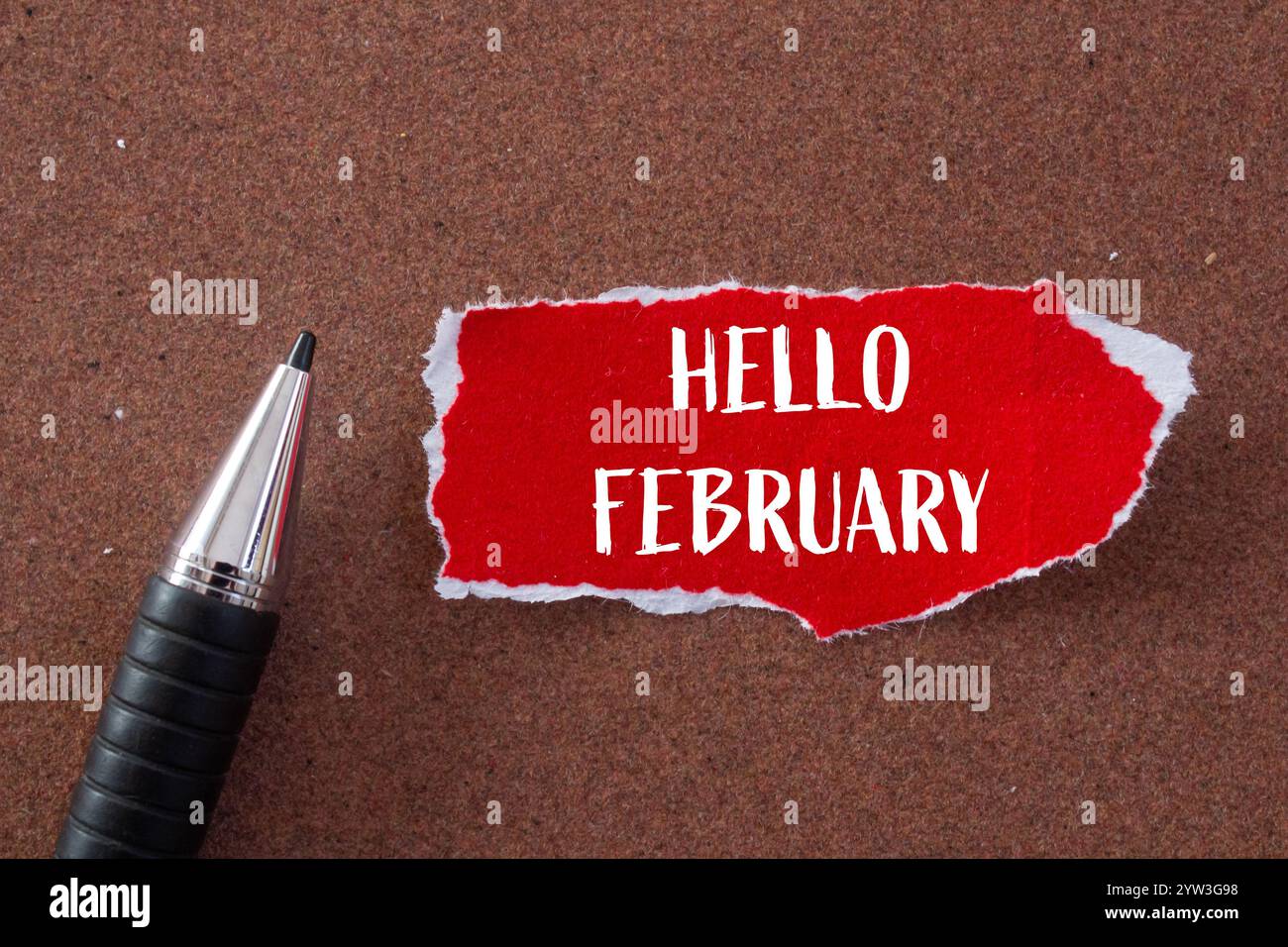 Bonjour février message écrit sur un morceau de papier rouge déchiré déchiré et un stylo avec fond brun. Symbole conceptuel bonjour février. Copier l'espace. Banque D'Images
