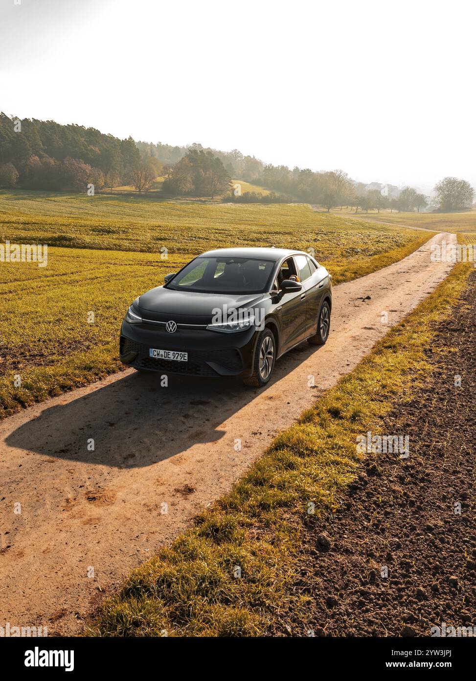 Une voiture sur une voie de campagne, flanquée de champs verts dans la lumière tôt le matin, voiture électrique VW ID5, Deer Carsharing, Gechingen, Forêt Noire, Allemagne, E Banque D'Images