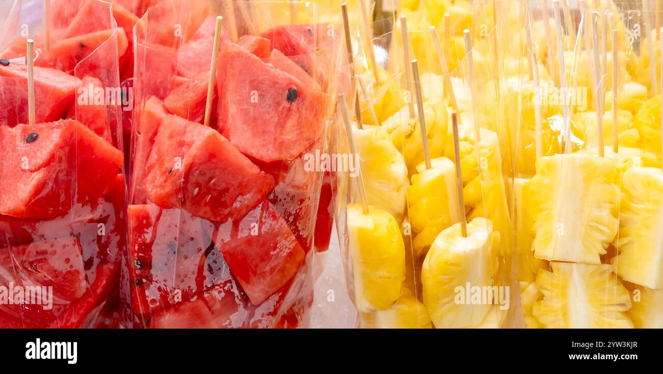 Plein cadre de pastèque rouge et d'ananas jaune en morceaux ou en tranches dans un sac en plastique transparent sont en vente au stand de nourriture de rue. Banque D'Images