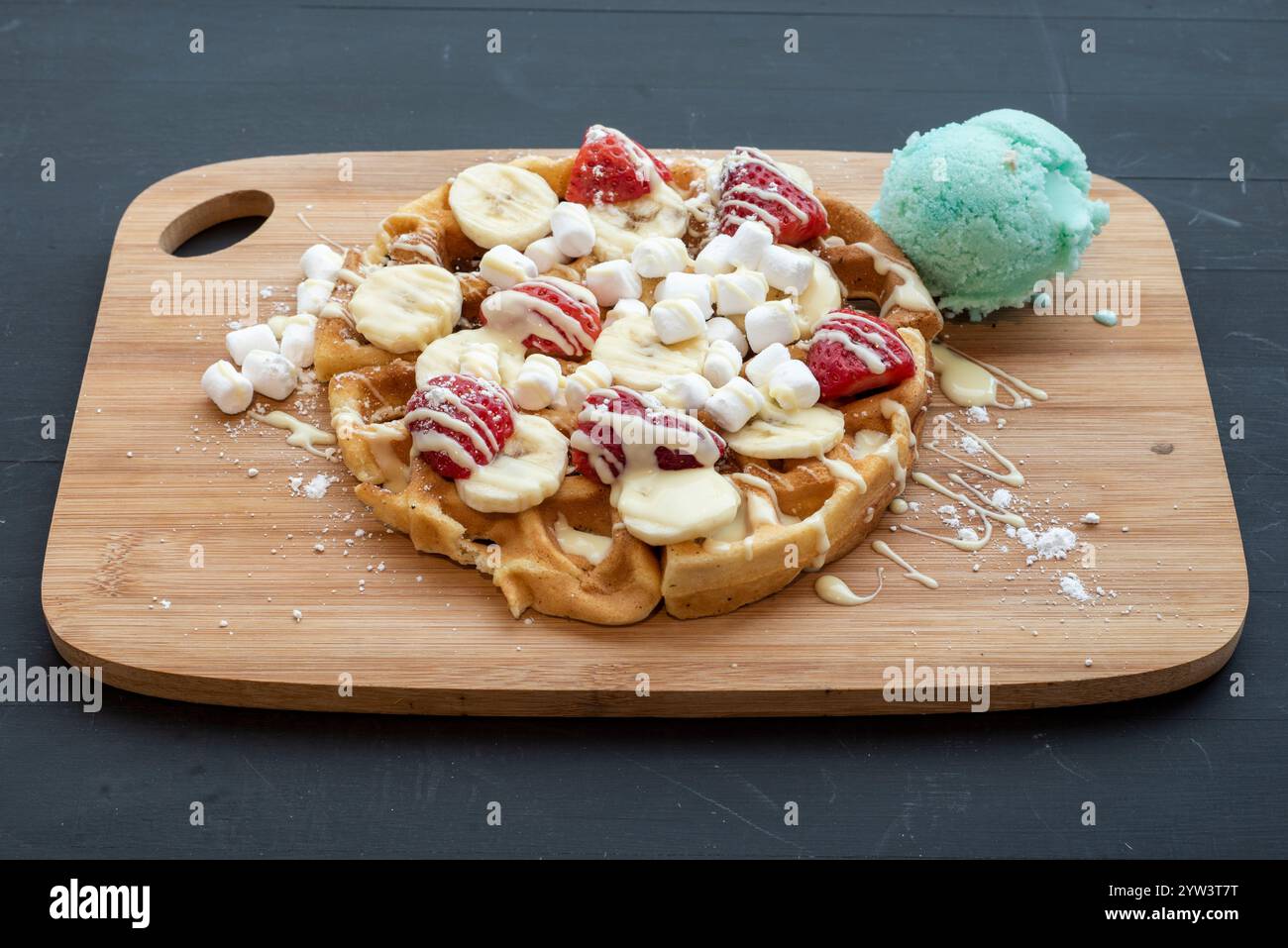 Délicieuse gaufre à la banane et à la fraise servie avec de la crème glacée et un filet de sauce au chocolat blanc Banque D'Images
