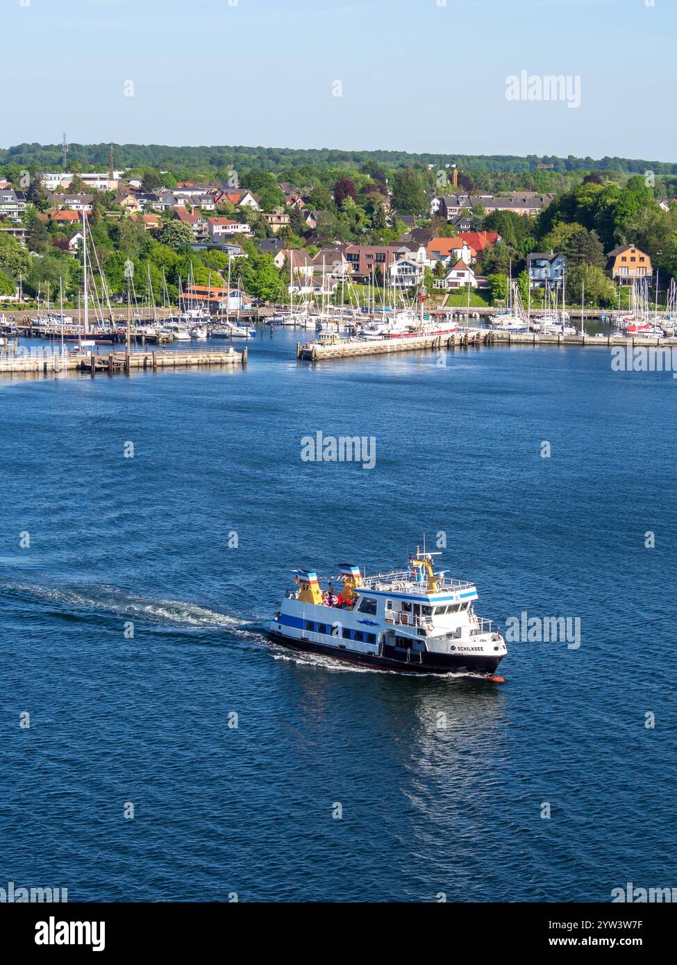 Vue en hauteur de Schilksee, un petit ferry traverse le fjord de Kiel par une belle journée d'été avec des yachts amarrés dans une marina et des bois derrière. Banque D'Images