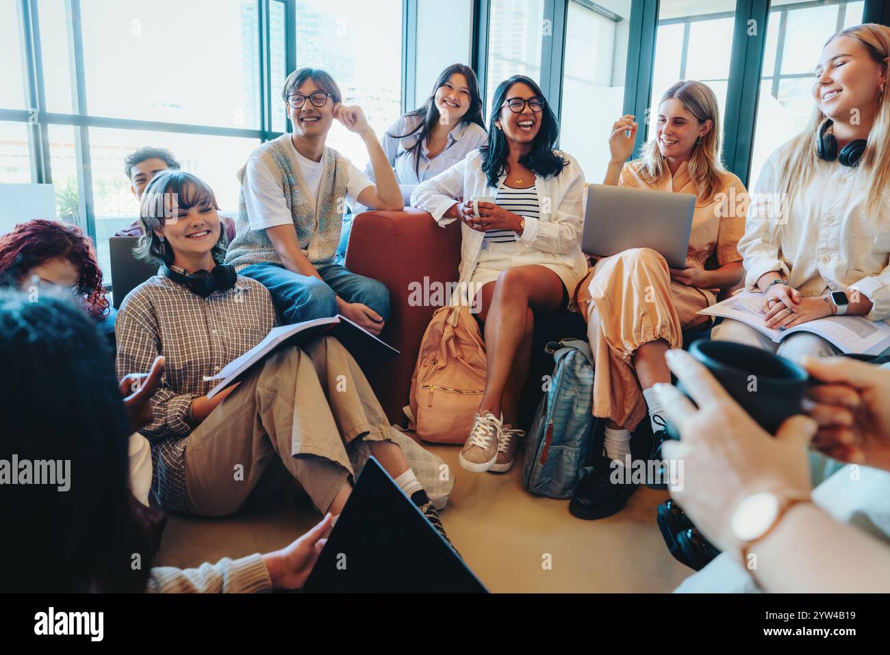 Un groupe d'étudiants divers dans une salle de classe décontractée, s'engageant avec des ordinateurs portables et du matériel d'étude. Ils partagent des idées et apprécient une collaboration Banque D'Images