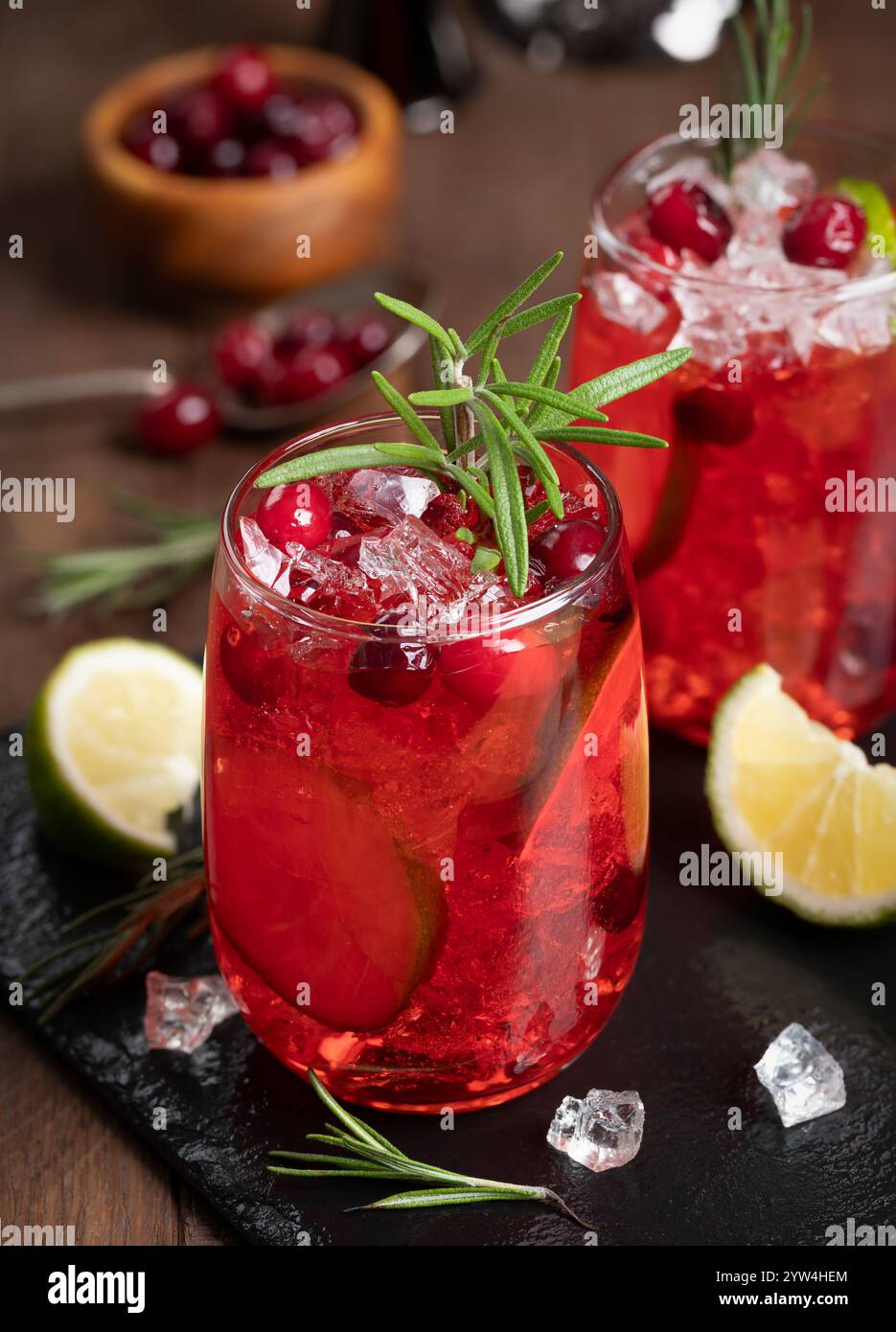 Cocktail de canneberges avec tranches de citron vert et glace pilée garnie de romarin sur planche d'ardoise noire avec fond en bois Banque D'Images