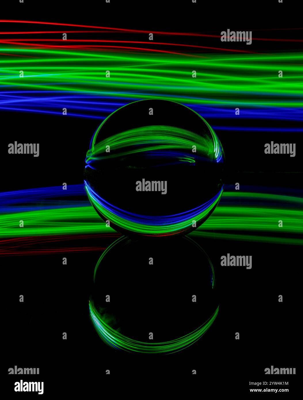 Traînées de lumière abstraites bleues, vertes et rouges créées par la peinture à la lumière autour d'une boule de verre statique posée sur un miroir sur un fond noir Uni Banque D'Images