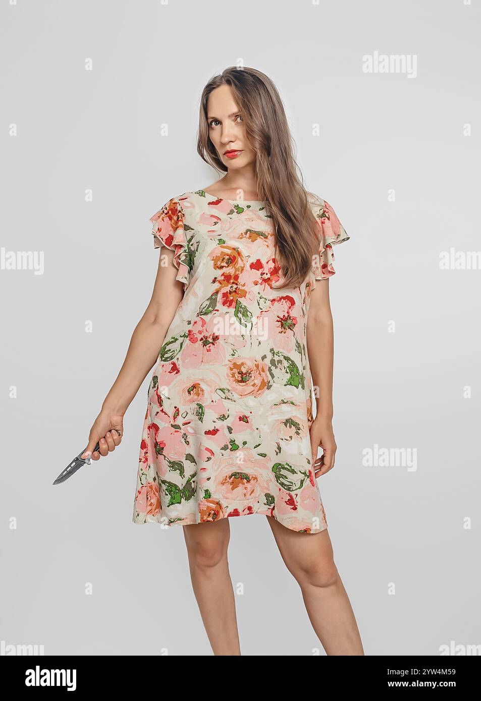 Femme dangereuse en robe d'été courte, tenant un couteau à la main, regardant menaçante la caméra. Fond blanc Banque D'Images