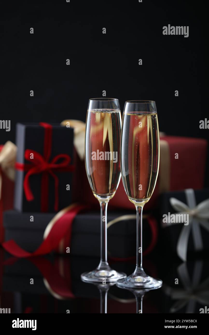 Délicieux champagne en verres et cadeaux de Noël sur la surface miroir noire Banque D'Images