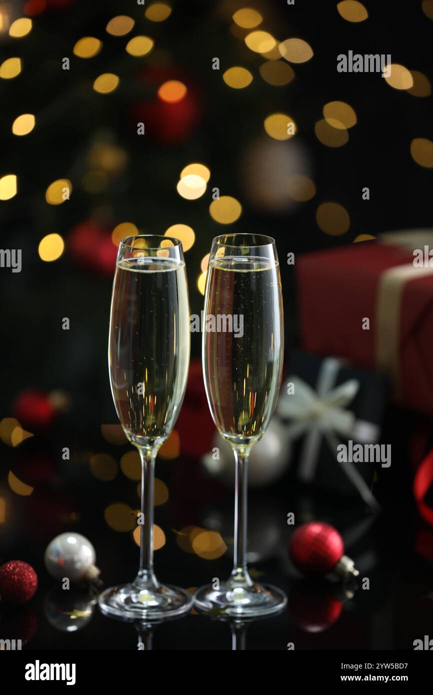Délicieux champagne dans des verres et décor de Noël sur la surface du miroir noir contre les lumières floues, gros plan Banque D'Images