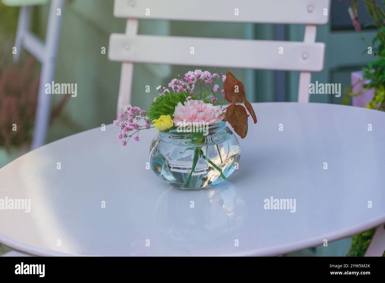 Un petit vase en verre avec des fleurs se dresse sur une table dans un café d'été. Banque D'Images