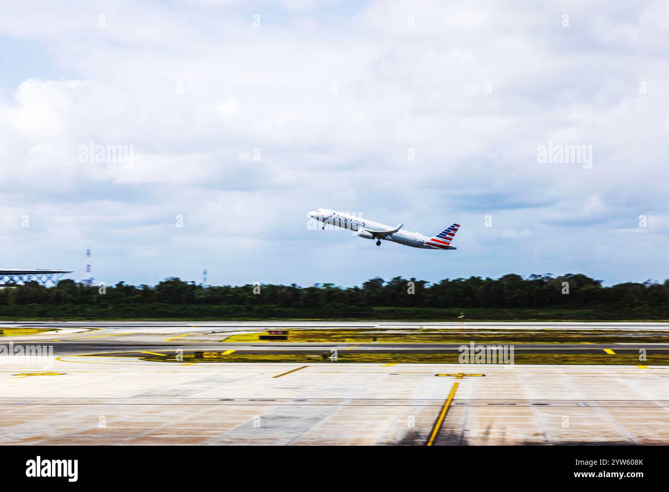 Avion American Airlines décollant de la piste de l'aéroport sous ciel nuageux avec la verdure environnante. Cancun. Mexique. Banque D'Images