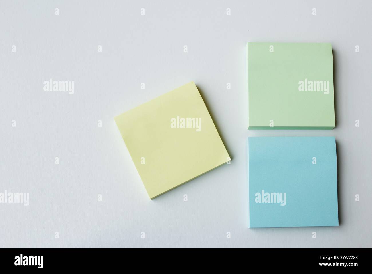 Trois blocs-notes adhésifs carrés de couleur pastel sur fond blanc avec espace de copie. Papeterie créative pour l'étude, le brainstorming, les réunions de bureau et l'école Banque D'Images