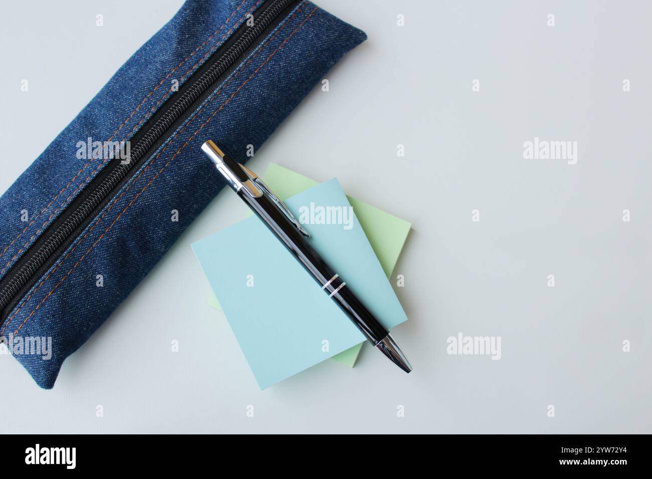 Étui à crayons en tissu denim, stylo à bille et notes adhésives de couleur pastel sur fond blanc avec espace de copie. Fournitures scolaires, papeterie, étudiant. Banque D'Images