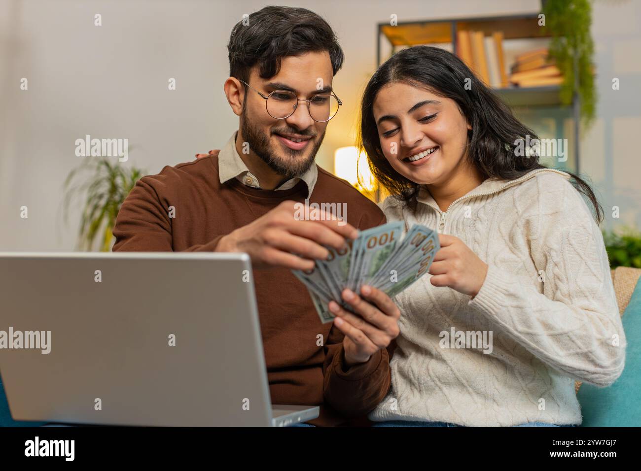 Heureux jeune couple hispanique comptant de l'argent et des billets de réservation pour des vacances se trouve sur le canapé dans le salon à la maison. Famille diversifiée détenant des billets de banque planification de budget d'investissement en ligne Home Finance Banque D'Images