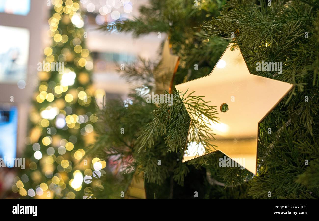 Décoration festive d'une étoile dorée accrochée sur l'arbre avec arbre de Noël éclairé à l'arrière-plan. Banque D'Images