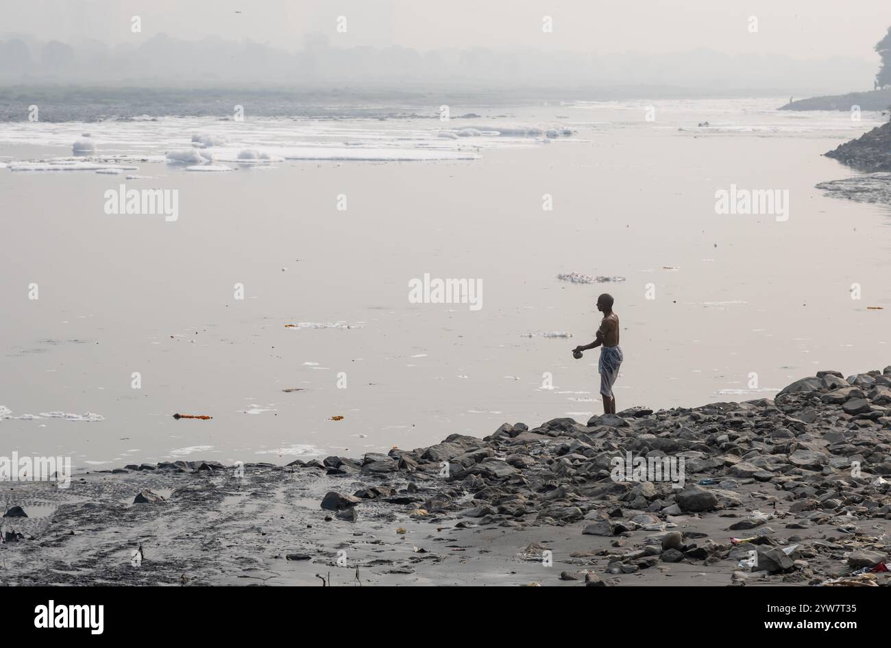 Homme isolé exécutant des rituels sacrés dans la rivière polluée avec de la mousse toxique au matin brumeux Banque D'Images