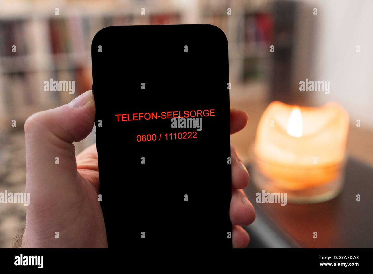 Téléphone portable avec le numéro de téléphone du service de conseil téléphonique dans une main dans un salon Banque D'Images
