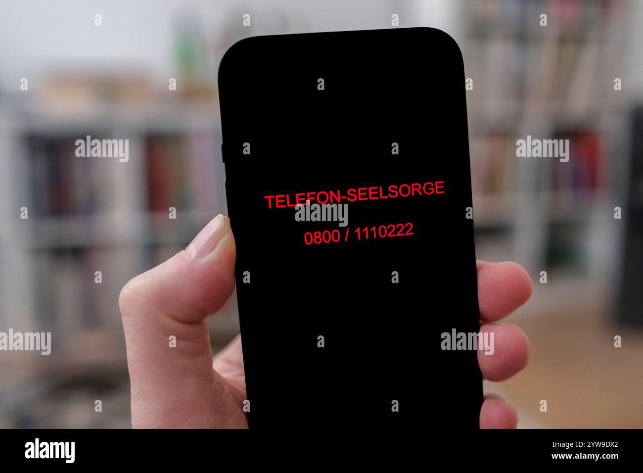 Téléphone portable avec le numéro de téléphone du service de conseil téléphonique dans une main dans un salon Banque D'Images