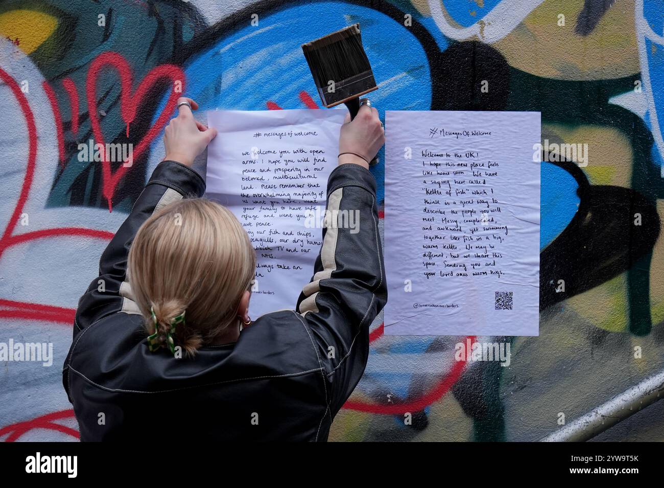 Colette Batten-Turner, PDG de conversation Over Borders, place des affiches avec le message de Noël « Un message de bienvenue » dans la ville de Brighton, dans l'est du Sussex, dans le cadre d'une campagne nationale de l'organisation caritative de réfugiés conversation Over Borders. Des centaines d'affiches présentant des messages manuscrits de compassion envers les demandeurs d'asile sont affichées dans tout le pays à l'approche de Noël dans le cadre d'une campagne nationale visant à créer un «environnement accueillant pour tous» au lendemain des émeutes d'été. Date de la photo : mardi 10 décembre 2024. Banque D'Images