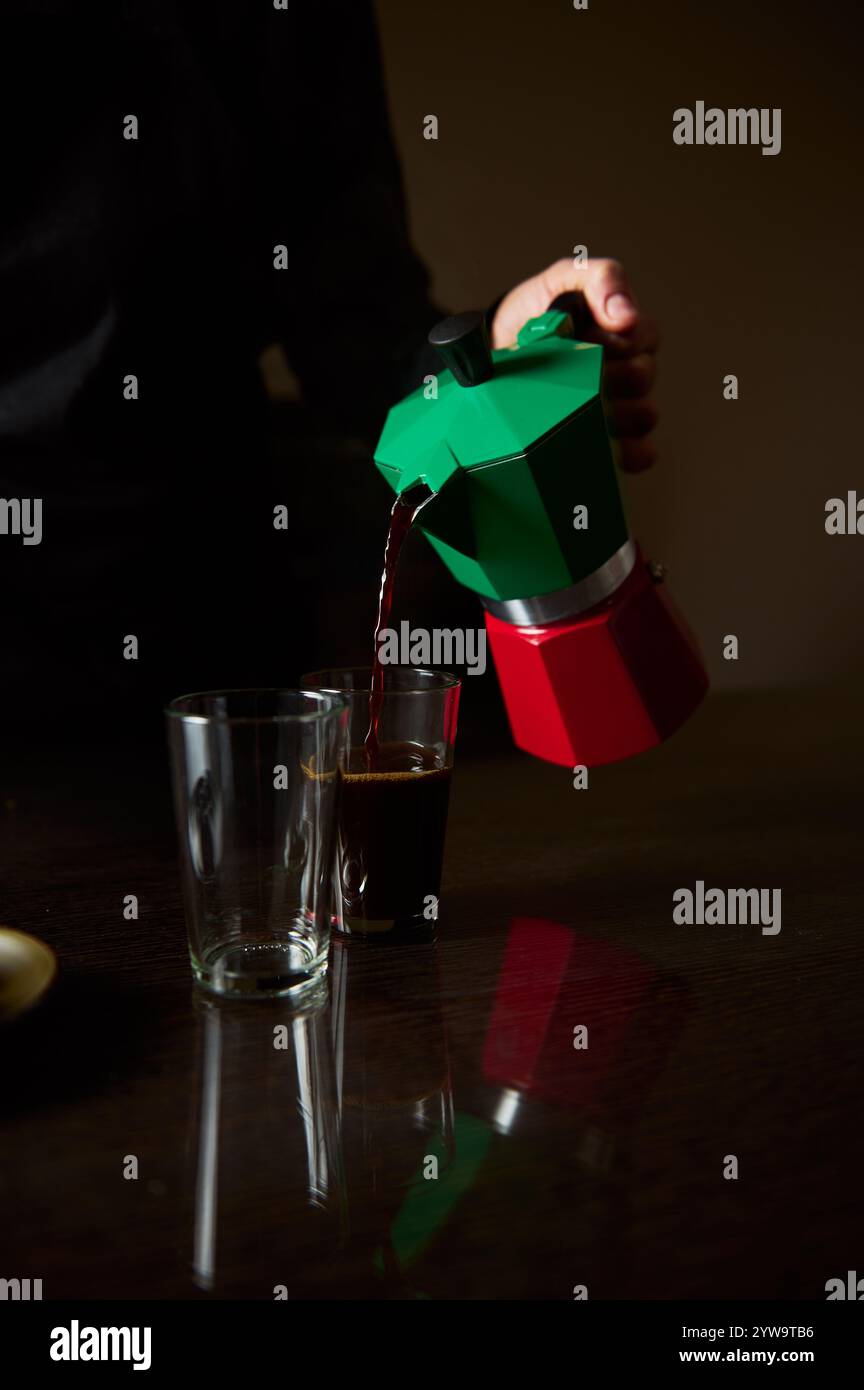 Gros plan du café versé d'un pot de moka dans un verre. La scène est chaleureuse et accueillante, mettant l'accent sur le plaisir d'un café fraîchement infusé dans un Banque D'Images