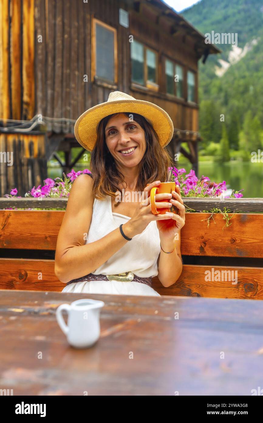 Femme portant un chapeau de paille appréciant une boisson chaude dans un chalet de montagne au bord du lac dans les dolomites italiennes Banque D'Images