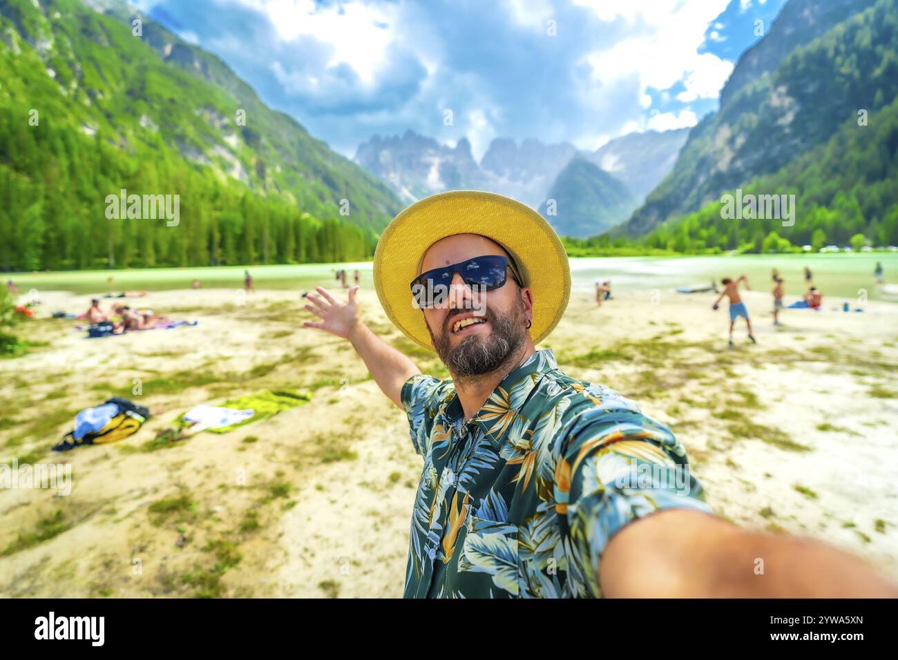Homme heureux dans une chemise hawaïenne et chapeau de paille prenant un selfie au lago di Landro, avec des touristes et tre cime di lavaredo en vue Banque D'Images