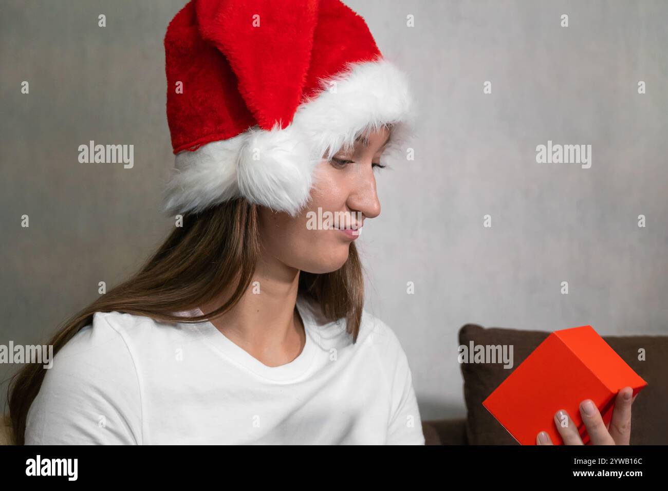 Femme triste portant chapeau de père noël ouvrant la boîte cadeau de noël à la maison, exprimant sa déception avec le cadeau qu'elle a reçu Banque D'Images