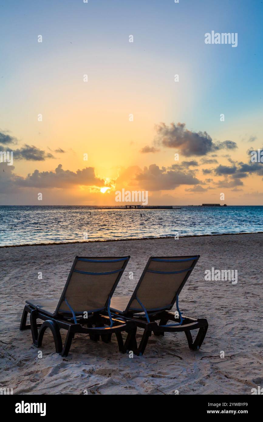 Deux chaises de plage sont face à l'océan, avec le coucher de soleil en arrière-plan. Les chaises sont vides, et la scène est paisible et sereine Banque D'Images