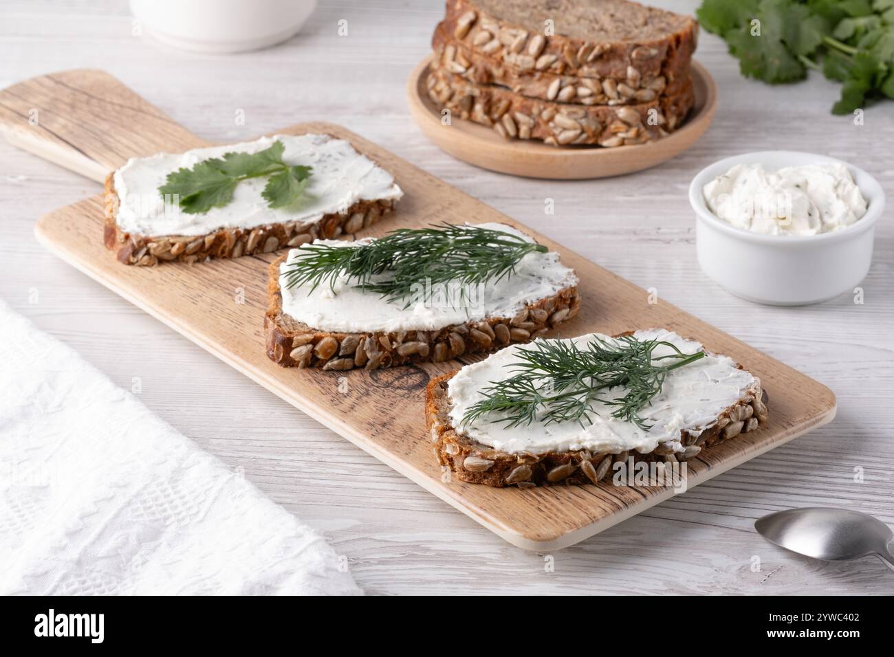 Tranches de pain de grains entiers fraîchement préparées, recouvertes de tartinade crémeuse et garnies de coriandre sur une planche à découper en bois. Banque D'Images