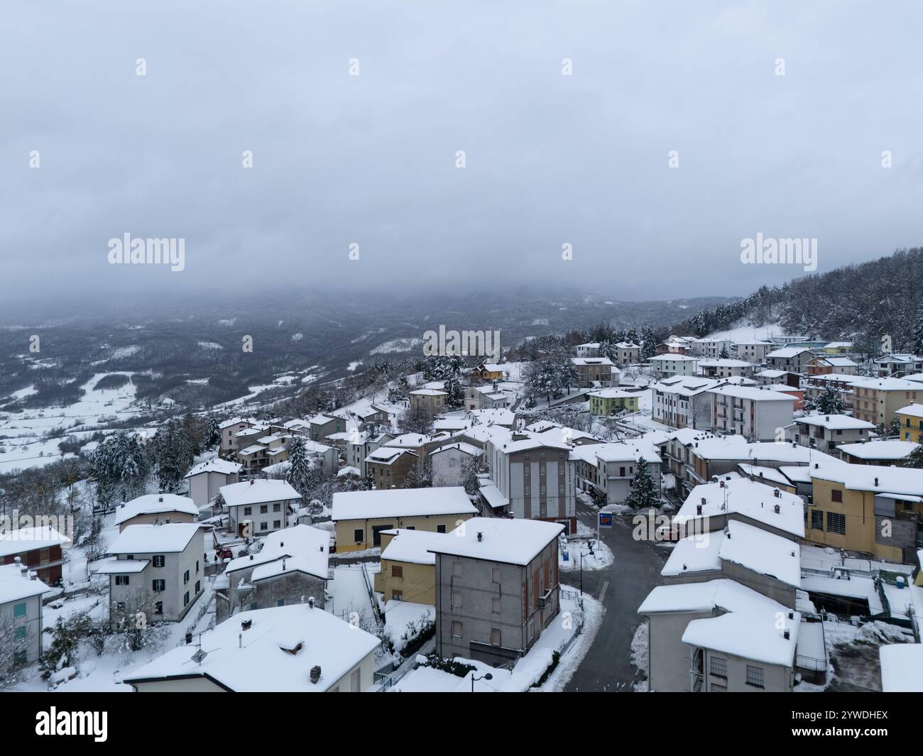 Vue aérienne capturant un village enneigé niché dans les montagnes par une journée nuageuse d'hiver, évoquant une atmosphère tranquille et sereine au milieu du froid Banque D'Images