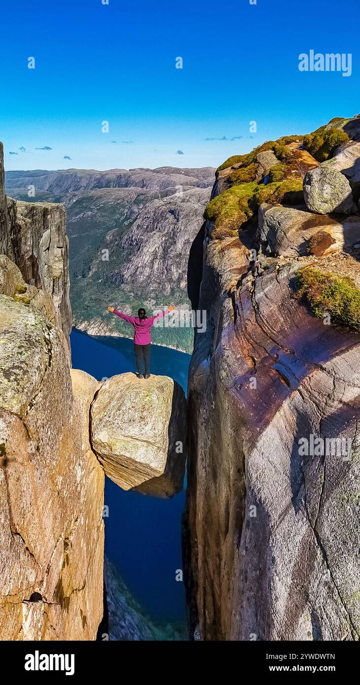 Un randonneur solitaire se tient au bord de la falaise de Kjeragbolten, Norvège, profitant de la vue imprenable sur le fjord ci-dessous. Les femmes asiatiques visitent Kjeragbo Banque D'Images