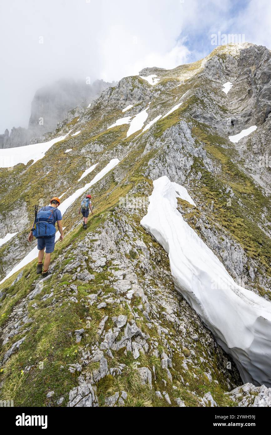 Deux alpinistes avec des casques sur un sentier de randonnée étroit, ascension à l'Ackerlspitze, nuages se déplaçant autour des montagnes, Wilder Kaiser, Kaiser Mountain Banque D'Images
