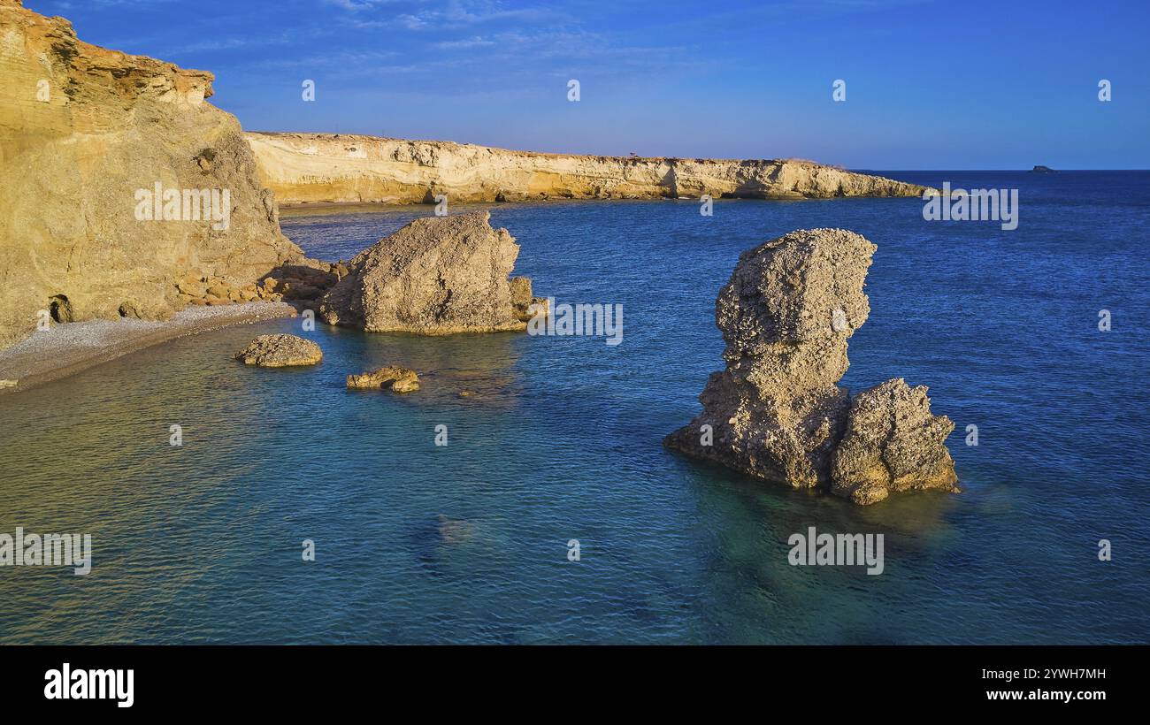 De grandes formations rocheuses s'élèvent de la mer bleu turquoise calme sous un ciel clair, tir de drone, lumière du soir, Araki Beach, côte sud-ouest, Karpathos, D. Banque D'Images