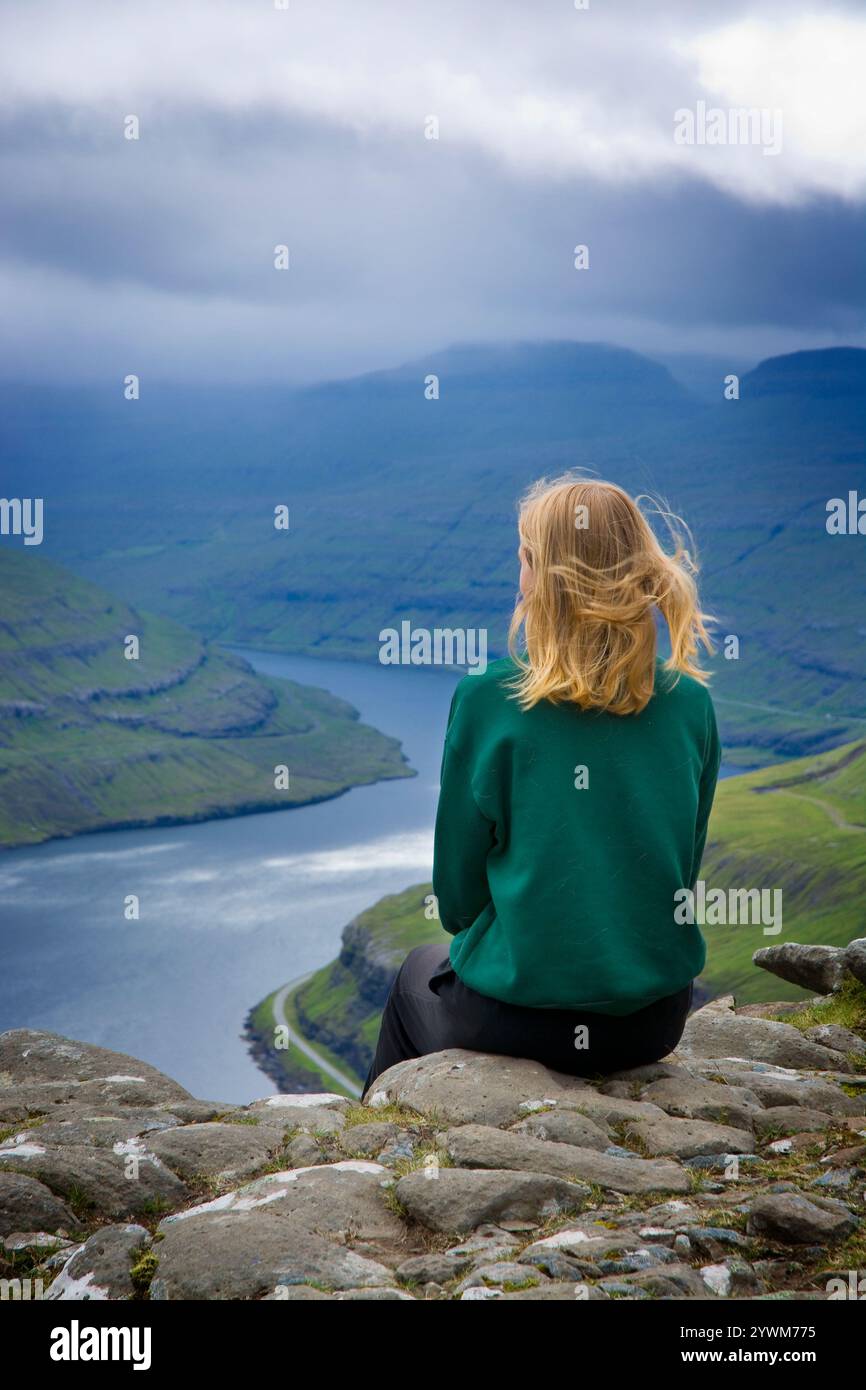 Fille méconnaissable assise près du Funningfjordur dans les îles Féroé. Vue depuis le point de vue Hvíthamar. Banque D'Images