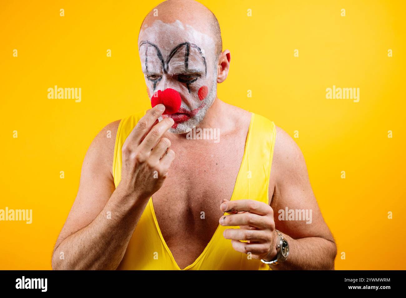Triste clown appliquant le maquillage sur fond jaune. Banque D'Images