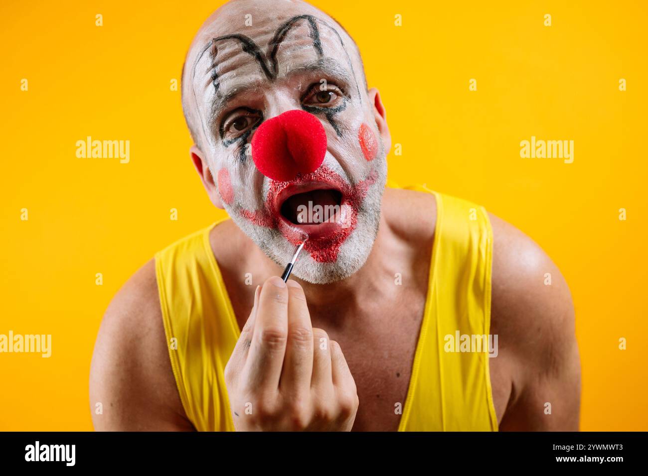 Triste clown appliquant le maquillage sur fond jaune. Banque D'Images