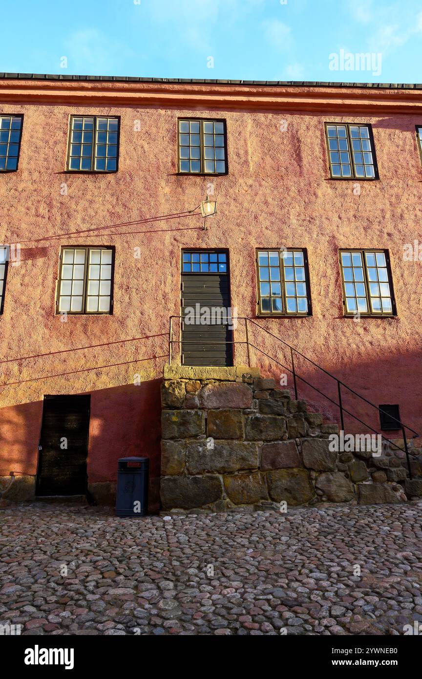 Un bâtiment rose comporte plusieurs fenêtres et une porte noire qui mène à une entrée surélevée. La structure se trouve bien en évidence dans une cour pavée Banque D'Images